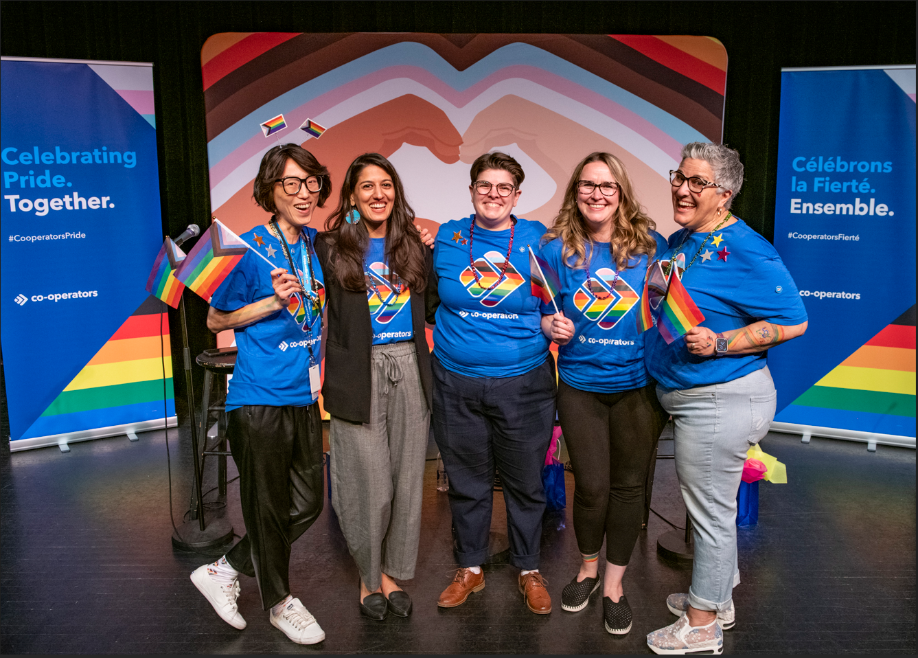 A group of people wearing blue shirts holding pride flags